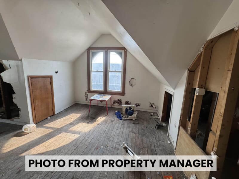 Upper-level room at 4900 Curtis Avenue featuring vaulted gable ceiling, double windows, exposed wood flooring, and unfinished wall openings.