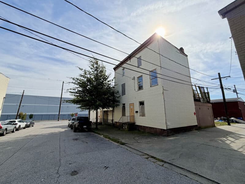 Rear and side exterior of 4900 Curtis Avenue in Baltimore showing the multi-story building, vinyl siding, elevated wooden deck, and alley access.