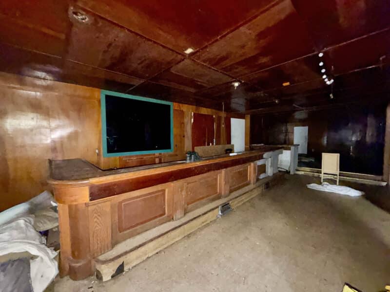 Interior of former tavern at 4900 Curtis Avenue featuring a long wooden bar counter, paneled walls, and commercial space requiring renovation.