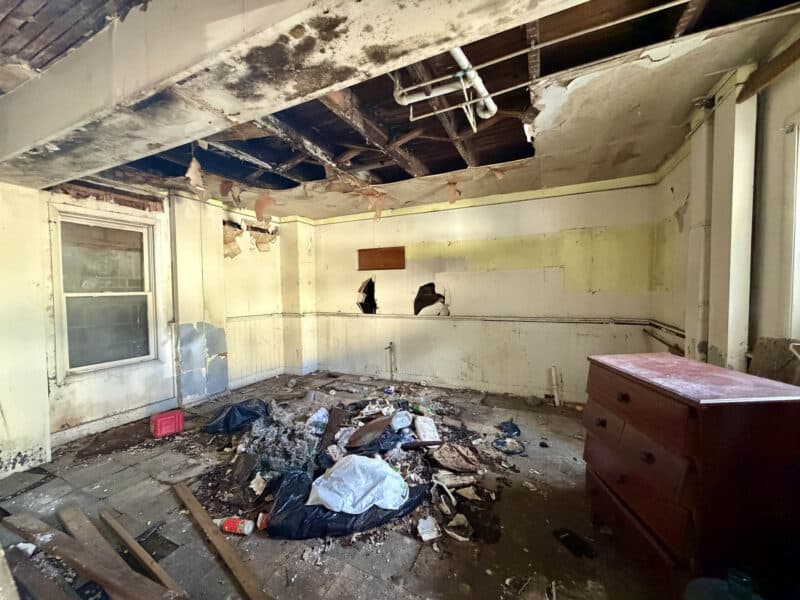 Interior renovation area at 4900 Curtis Avenue showing exposed ceiling joists, damaged plaster, debris, and deteriorated walls.